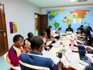 Members studying the Bible together around a long table, with notebooks and Bibles open